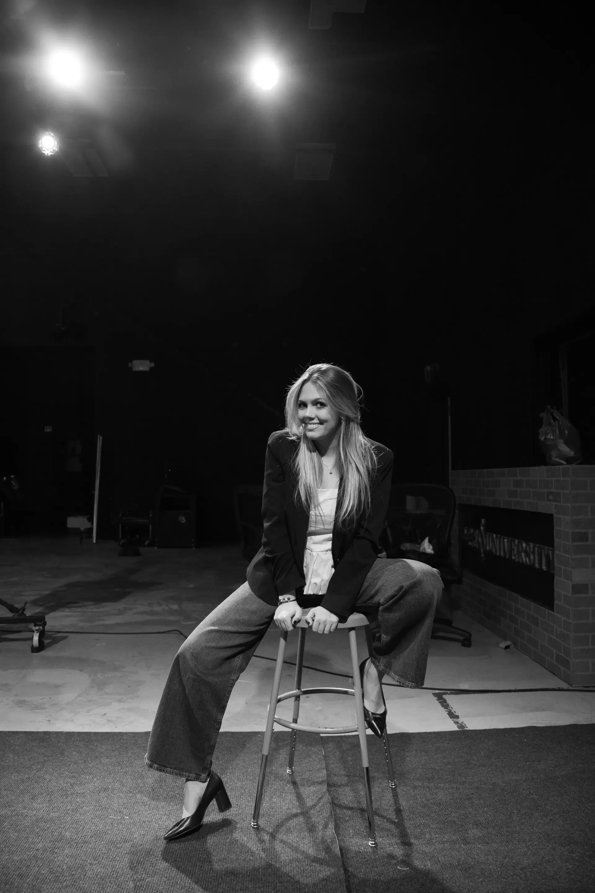 Mariana Michalek seated on a stool on a dark stage, in black and white